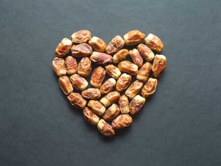 Dates fruit are laid out in the shape of a heart on a black table.
