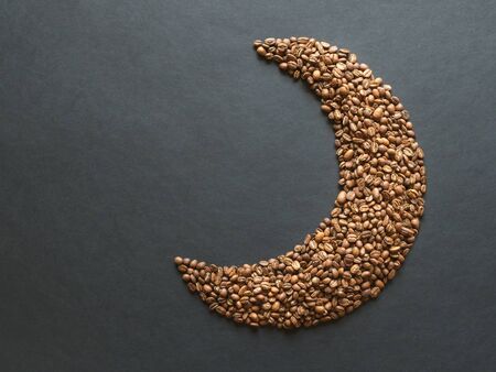 Coffee beans are laid out in the shape of a Crescent on a black table.の写真素材
