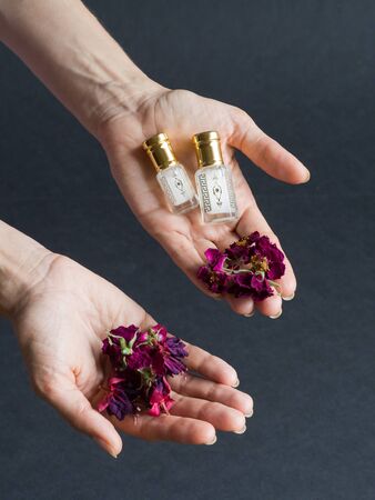 Concentrated essential oil in a mini bottle in the hand with floral petals on the black background.の写真素材