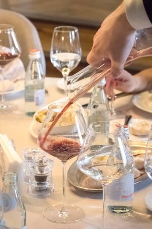 Waiter pours a glass of wine from the decanter during dinner. Close up.