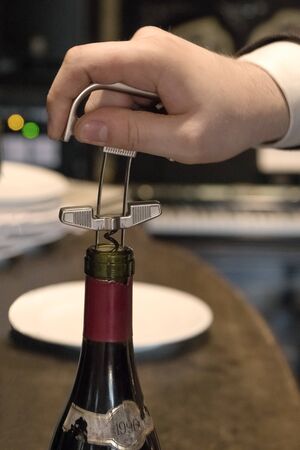 The waiters hand opens a bottle of vintage wine with a corkscrew. Close up.の写真素材