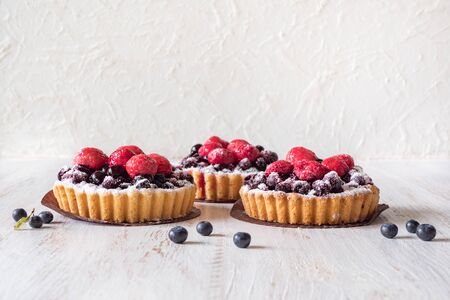 Beautiful delicious tarts, colorful pastry cakes sweets with fresh raspberries and blueberry on white wooden background.の写真素材