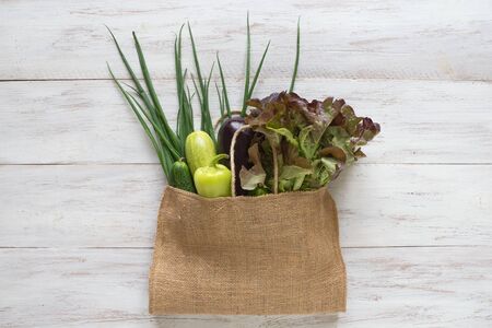 Vegetables in a grocery bag on a wooden table.の写真素材