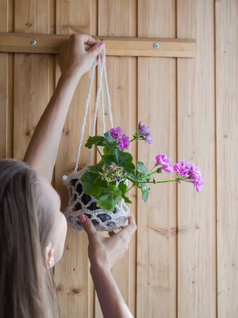 A woman hangs a pot with a potted plant on the wall. Indoor floriculture.の写真素材