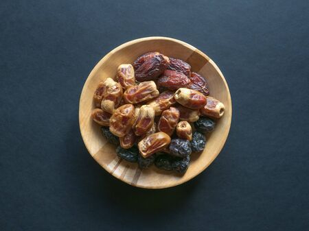Dates in a wooden bowl on a black background. Top view.の写真素材