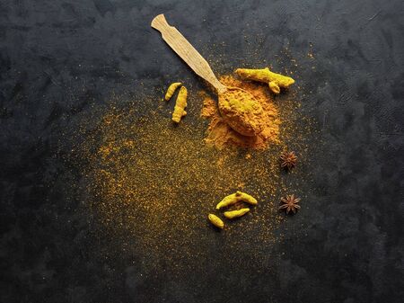 Turmeric powder and roots turmeric on black background. Ingredients of ayurvedic treatment. A remedy for viruses and many diseases.の写真素材