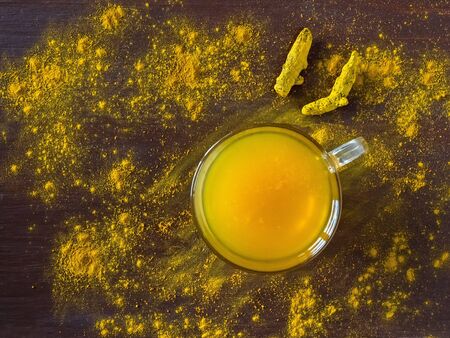 Herbal tea with turmeric powder and turmeric roots on a brown table. Prevention of antiviral...