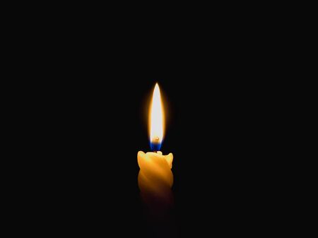 A burning candle on a dark background.
