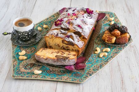Homemade cake with dates and nuts, served with black coffee on a white wooden table.
