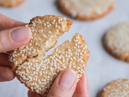 Hand breaks fresh delicious sesame cookies. Close up.