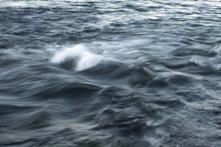 The stream of water, blurred view. Powerful water flow with breakers on the sea.