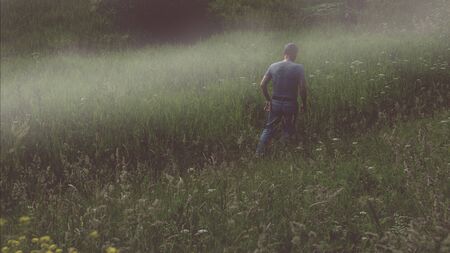 A mysterious male figure walking away in a foggy field in summer with a dark muted edit.の写真素材