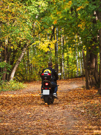 A biker on a motorcycle rides along a forest road with a backpack on his back. Picnic in nature.の写真素材