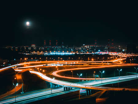 Moonlight over a night road junction in an industrial area of a modern metropolis. Aerial view. Long shutter speed with blurred lights from the headlights.の写真素材