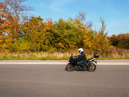 Motorcyclist in motion. Woman biker on a black motorcycle in traffic on a rural autumn roadの写真素材