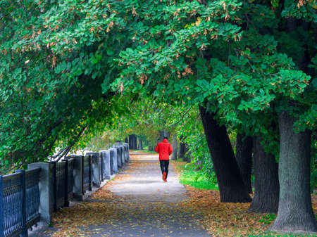 A man in a red sports windbreaker runs down a deserted street early in the morning. Morning fitness run on the embankment in Moscowの写真素材