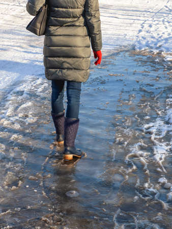 Ice-crusted ground, a woman walking on a slippery street, spring weather. Icy conditionsの写真素材