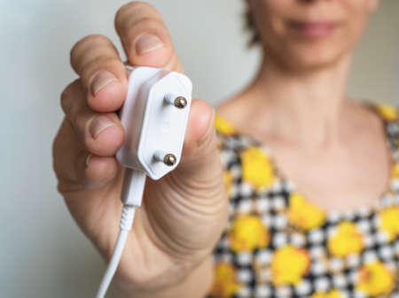 Woman hand holding Electric plug. Close up. Earth Hour saving electrical energy.