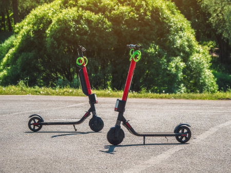 Two city scooters on the asphalt. Two parked scooters in the summer city. Modern youth mode of...