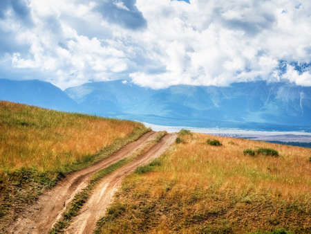 Way through mountains. Trekking mountain trail. Bright atmospheric minimalist alpine landscape with stony footpath among grasses in highlands. Pathway uphill. Way up mountainside.の写真素材