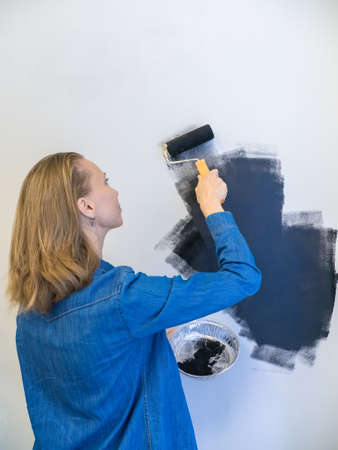 Selective focus. Pretty woman with a roller paints the wall black. Home repair concept. Copy space.の写真素材