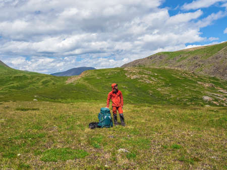 Tired tourist sits on a large backpack and happily looks into the distance against the background of...