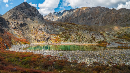 Solo traveler in a yellow raincoat on the trail.Panoramic colorful landscape with footpath along water streams in valley in autumn colors with view to autumn mountains and rocks in golden sunshine.の写真素材