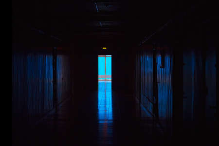 Blue light at the end of a dark corridor. End of dark tunnel with magic blue light. Empty dark corridor in hospital laboratory.の写真素材