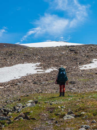 Vertical view solo trekking in the mountains. Man with a large backpack is climbing heavily on a mountain trail. Adventure solo traveling lifestyle concept, active weekend vacations on the wild natureの写真素材
