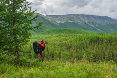 Vertical view solo trekking in the mountains. Man with a large backpack is climbing heavily on a mountain trail. Adventure solo traveling lifestyle concept, active weekend vacations on the wild natureの写真素材