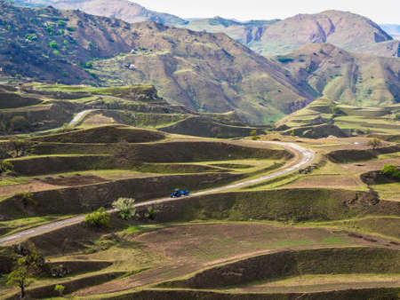 Dirt road to a distant mountain village. Spring view of the city on the rock. Authentic Dagestani...