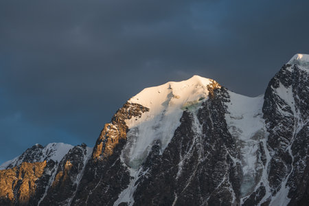 Awesome scenery with sunlit snow mountains in cloudy sky at sunrise. Dark scenic landscape with...