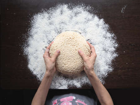 Baker's hand holds the raw yeast-free dough on a dark background. white bread texture. Mankind...