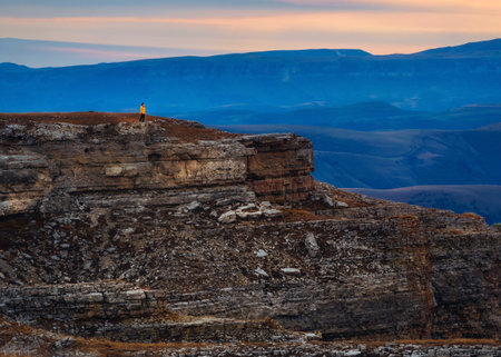 Contrasting mountains at sunrise. Purple sunrise over majestic Bermamyt plateau. Sunset in magenta tones. Tourist walks on mountain near abyss edge on high altitude.の写真素材