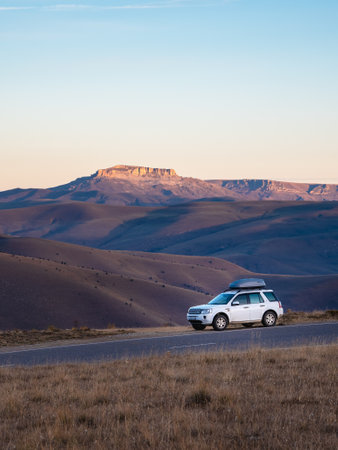 Russia. Kabardino-Balkaria. October 2022. White car SUV is parked next to a scenic route road in a morning autumn landscape near Bermamyt plateau. Luggage trunk box mountain on car roof rack.のeditorial素材