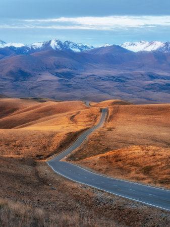 Vertical view of a picturesque road stretching into the distance through the picturesque autumn hills. Winding asphalted clean road stretches into the distance to the snow-capped mountains.の写真素材