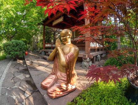 Bronze Gautama Buddha decorative statue in a garden under red maple leaves. Outdoor garden decor concept. Abakan.の写真素材