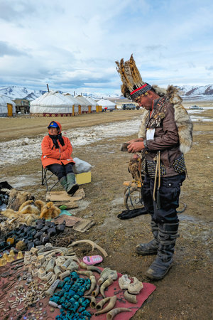Ulgiy, Mongolia - October, 01, 2023: Kazakh in a hat made of feathers. Sale of homemade bone products with traditional ornaments. Kazakh outdoor market. Travel to the Mongolia. Vertical view.のeditorial素材