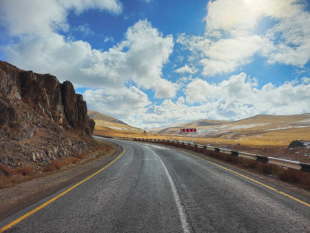 Asphalt mountain track, turn on the road. Beautiful autumn high-mountain highway with twisting turns. Rocky mountain landscape in the background during a white cloudy autumn morning. Mongolia.の写真素材