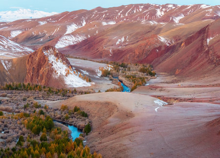 Scenic motley autumn landscape with yellow larch trees on frozen red hills, blue river and mountain...
