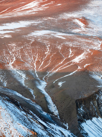 Vivid multicolor nature background of colorful highland valley among big rocky mountains. Snow surface of giant red mountain rough wall and green valley. Red orange yellow rocks. Vertical view.の写真素材