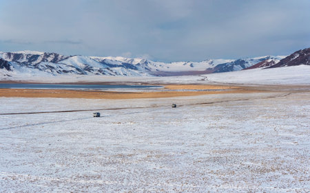 Wide winter steppe, a narrow road, cars driving across the plateau on a narrow dirt road. The wide...