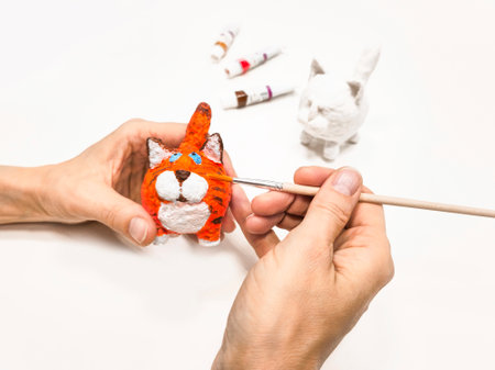 Creating a handmade toy. Cheerful wadding toy cats by handmade. Painting with a brush funny red cat,...