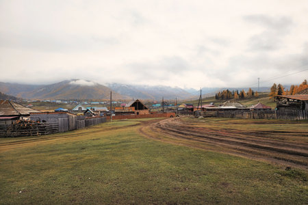 Autumn dirt road from a hill to a remote village. Off-road, dirt road up the slope in a remote woodland with yellow autumn larches. Mountain autumn off-road track to high mountain village.の写真素材