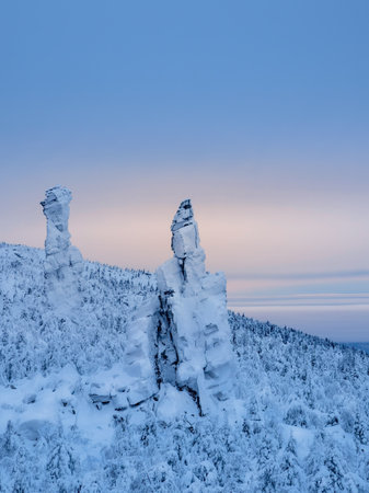 Rock pillars, weathering posts. High stone cliff covered with snow and rise above the coniferous forest at sunset. Perm region, vertical view.の写真素材