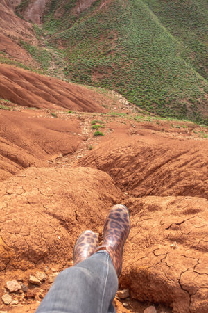 Feet over the cliff. Hanging legs over cliff over red slope.