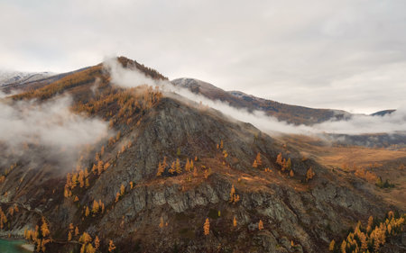 Pyramidal mountain with rocks and autumn forest mountains covered by clouds. Best place for active...