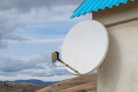 Satellite antenna on the white house wall and blue cloudy sky. TV - receiver on the house wall.の写真素材