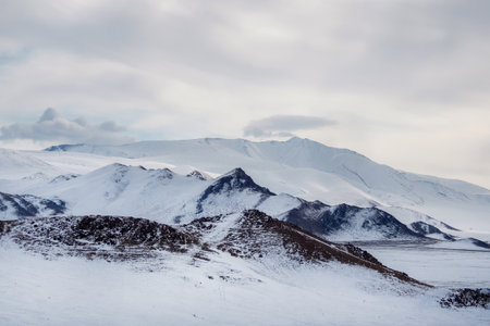 Cold snow-white landscape of snowy valley. Snow-covered rocky mountain range under clouds in blue sky. Pure white snow in high mountains in sunny day.の写真素材