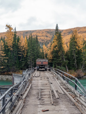 Old truck driving on a dilapidated bridge over a river. Remote area of Gorny Altai in autumn. Logging. Vertical view.の写真素材
